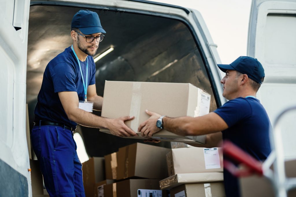 Young couriers cooperating while unloading packages from deliver